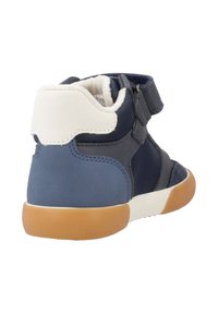 Zapatilla alta de color azul marino con un talón blanco en contraste, correa de velcro y suela de goma. Presenta una mezcla de materiales texturizados.