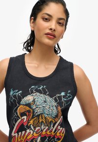 Canotta nera in cotone con grafica di un'aquila colorata e audace scritta "Superdry", con scollatura a giro e design senza maniche.