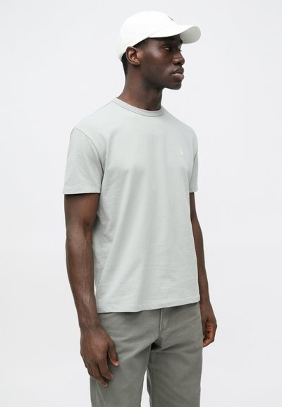 Svetlosivé bavlnené tričko s okrúhlym výstrihom a krátkymi rukávmi, s malým logom na hrudi. Kombinované so sivými nohavicami.