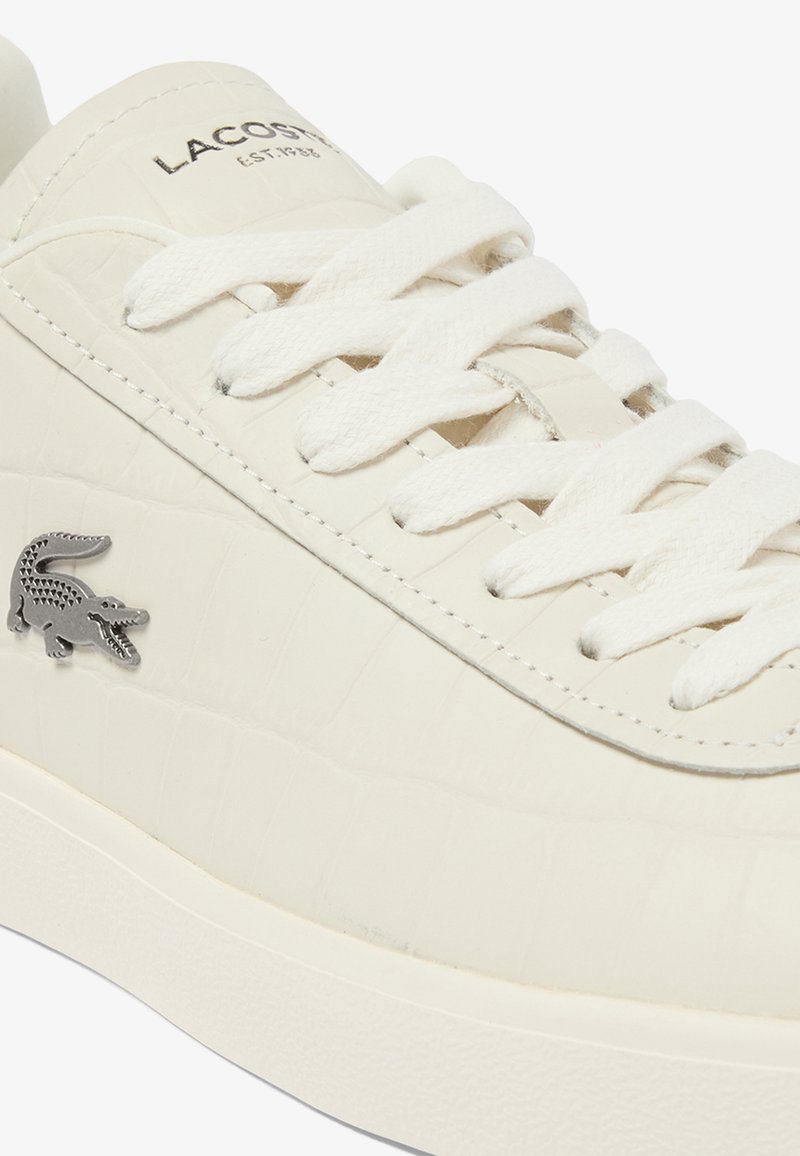 Sneaker in pelle vegana bianca con motivo a coccodrillo testurizzato, con lacci bianchi piatti e logo coccodrillo argentato sul lato.