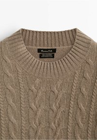 Beige Kaschmirpullover mit Zopfstrickmuster, ausgestattet mit einem gerippten Rundhalsausschnitt und einem Etikett mit der Aufschrift "100% Kaschmir, hergestellt in Madagaskar."