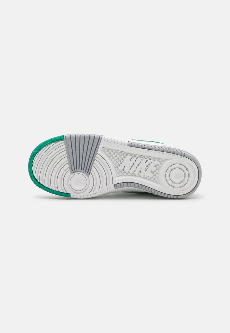 Semelle de chaussure Nike avec un design en caoutchouc texturé blanc, des accents verts et un motif de semelle circulaire distinctif.