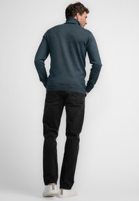 Granatowy sweter z dzianiny z wysokim kołnierzem, prążkowanymi mankietami i dołem, dopasowany do czarnych dżinsów i jasnych sneakersów. Minimalistyczny design.