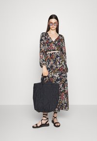 Vestido floral de manga longa com decote em V, em tons de azul-marinho e multicoloridos, combinado com uma bolsa de mão preta texturizada e sandálias pretas de tiras.