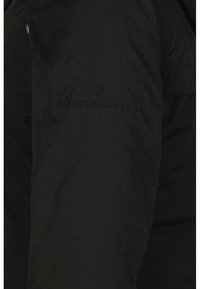Chemise noire à manches longues avec un logo « DreiMaster » brodé discret sur la poitrine, portée sur le torse d'une personne.