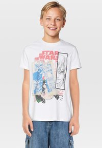 Camiseta de algodón blanca con gráfico multicolor de "Star Wars", que incluye ilustraciones y texto estilo cómic, con un diseño clásico de cuello redondo.