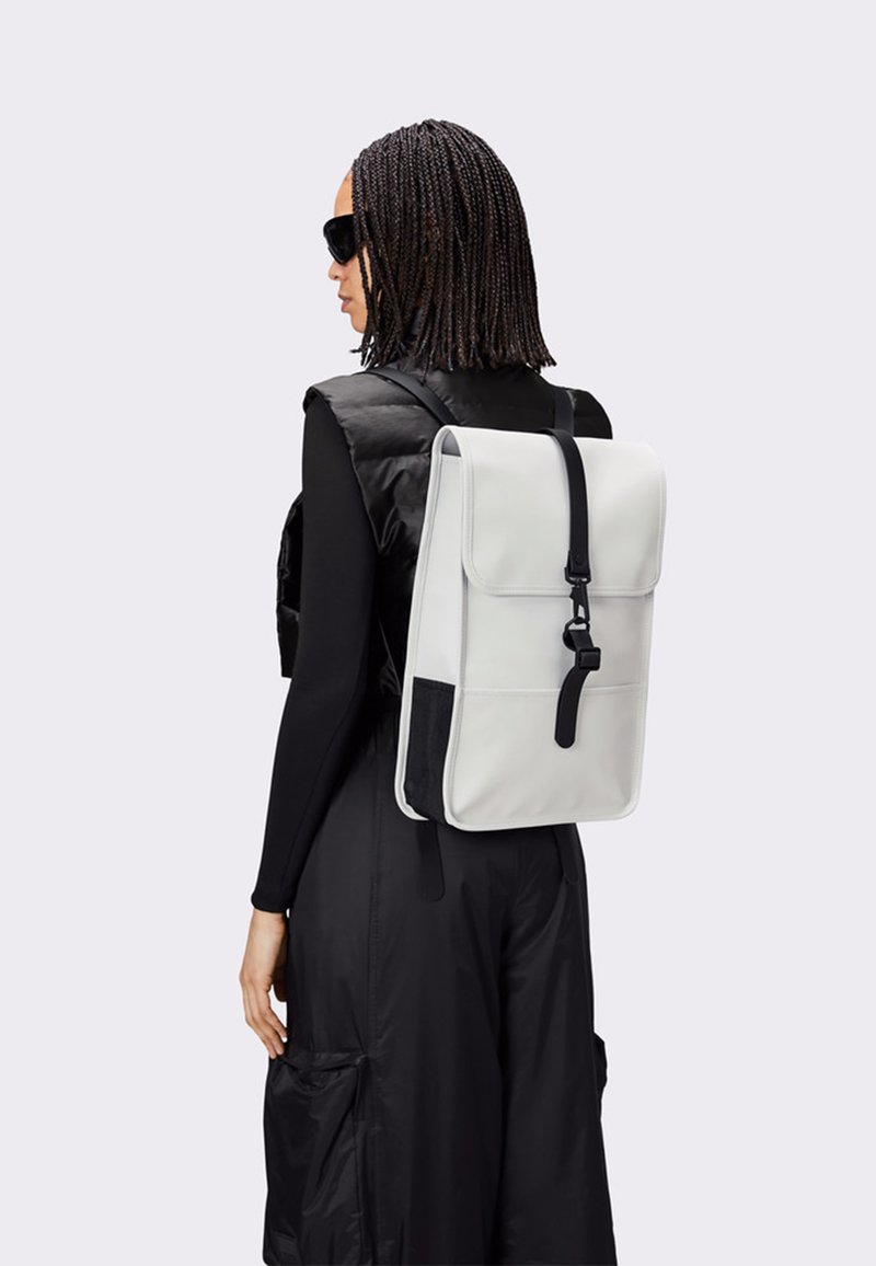 Vit läderryggsäck med en vikbar klaff, svarta accenter och justerbara remmar. Slät textur och strukturerad rektangulär form.