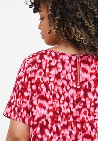 Κόκκινη και ροζ καπιτονέ μπλούζα με κοντά μανίκια, κλείσιμο με φερμουάρ στην πλάτη και χαλαρή εφαρμογή από υφασμάτινη ύφανση.