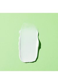 Weiße Creme oder Farbe, unregelmäßig in ovaler Form auf einem hellgrünen Hintergrund aufgetragen, zeigt eine glatte Textur und einen glänzenden Finish.