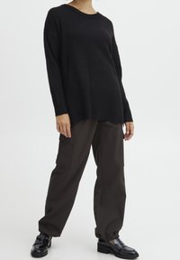 Czarny sweter dzianinowy z prążkowanym dołem, w połączeniu z luźnymi, ciemnobrązowymi spodniami cargo i błyszczącymi czarnymi butami, prezentującymi swobodny styl.