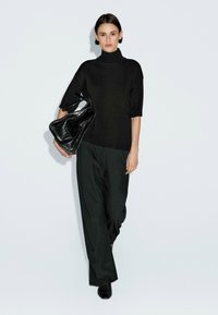 Maglione a collo alto nero lavorato a maglia con maniche corte, abbinato a pantaloni larghi verde scuro. Il modello tiene una borsa nera strutturata.