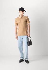 Tan polo majica z belimi detajli, gumbi spredaj, svetlo modri ravni jeans, črna kapa in majhna črna torbica čez ramo. Črni loaferji.