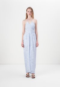 Lyseblå halter-neck kjole med tettsittende liv og strømpe skjørt, med et delikat blomstermønster og innsnørt midje. Akkompagnert av svarte sandaler.
