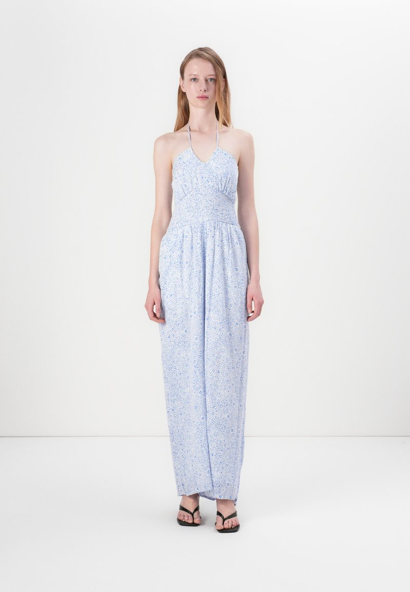 Lyseblå halter-neck kjole med tettsittende liv og strømpe skjørt, med et delikat blomstermønster og innsnørt midje. Akkompagnert av svarte sandaler.