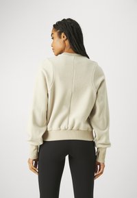 Lys beige fleece sweatshirt med rund hals, elastisk midjebånd og ribbed mansjetter. Har en søm nedover ryggen for ekstra detaljer.