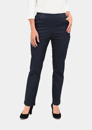Marineblaue elastische Hosen mit seitlichen Taschen, taillierter Schnitt und weichem Stoff. Getragen mit schwarzen High-Heels in einer stehenden Pose.