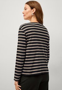 Chemise à manches longues rayée noire et beige avec une coupe décontractée. Texture douce, col rond et ourlet légèrement incurvé. Présente des détails de couture subtils.