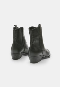 Botines negros de cuero con textura suave, cremalleras en la parte posterior y un tacón bajo. Diseñados con puntera redondeada y detalles de costura mínimos.