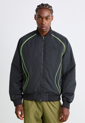 Black bomber jacket with lime green piping, front zipper, ribbed cuffs, and a zippered pocket on the left sleeve. Textured nylon fabric.
