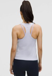 Débardeur de sport violet clair avec une finition texturée, design dos nu et fines bretelles, associé à un legging sombre. Vue de dos.