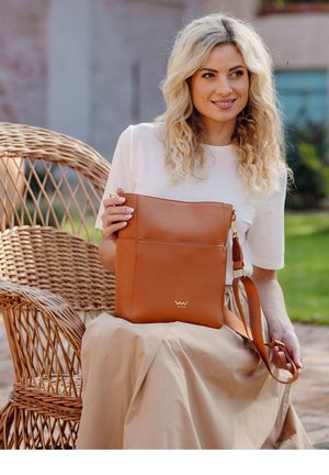 Tan leather shoulder bag with a smooth finish, featuring a front pocket, adjustable strap, and gold hardware accents. Simple design.