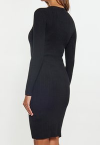 Robe en maille côtelée noire à manches longues, silhouette ajustée et ourlet au niveau des genoux. Texture lisse avec une légère élasticité pour le confort.