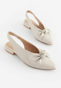 Beige slingback-kengät, jotka on valmistettu sileästä nahasta, teräväkärkiset ja edessä on solmittu nauha. Matala lohko korko.