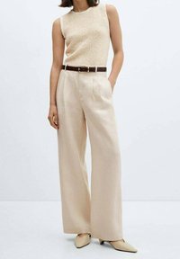Beżowy dzianinowy top bez rękawów i szerokie kremowe spodnie, dopełnione brązowym paskiem i spiczastymi beżowymi butami. Gładka faktura i luźny krój.