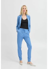 Chaqueta de traje azul claro y pantalones jogger a juego, con un top de encaje negro debajo. Los pantalones tienen una cinturilla elástica y bolsillos.