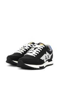 Scarpe da ginnastica nere con lacci bianchi e accenti grigi. Presentano una tomaia testurizzata, un collo imbottito e una suola in gomma nera spessa con un motivo a zigzag.