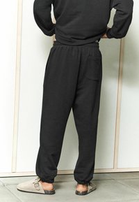 Zwarte sweatpants met een elastische tailleband en boorden, voorzien van een achterzak. Draag ze met lichtgrijze instappers. Minimalistisch ontwerp.