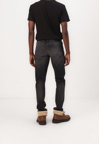 Jeans negros con corte ajustado, detalles desgastados y bolsillos traseros curvados, combinados con botas de tobillo marrones que presentan un puño de borrego.