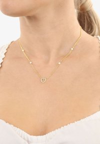Collana d'oro con catena a maglie, caratterizzata da piccole perle bianche e un pendente a forma di cuore circondato da pietre trasparenti.