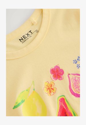 Żółta bawełniana koszulka z krótkim rękawem, zdobiona kolorowymi grafikami owoców i kwiatów, z okrągłym dekoltem i gładką teksturą. Metka marki widoczna wewnątrz kołnierza.