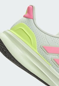 Zapatilla deportiva verde claro con parte superior texturizada, detalles en rosa y verde neón, suela de goma y diseño en capas para mayor estabilidad.