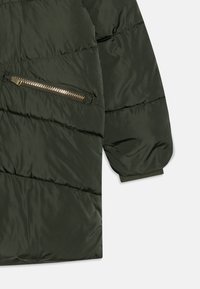 Zeleno, pustno quilted jakna s žeptanom na zadrgo. Gladko, sijajno blago z naborki na manšetah. Šivanje ustvarja vodoravni vzorec.