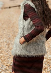 Faux fur vest in light gray with side pockets, layered over a burgundy ribbed long-sleeve dress with horizontal stripes.