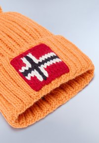 Berretto lavorato a maglia arancione con una texture a coste. Presenta una toppa con uno sfondo rosso e un design di croce bianca e nera.