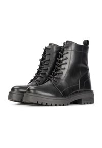 Bottes noires en cuir à la cheville avec un bout rond, un laçage à l'avant et une semelle en caoutchouc texturée. Elles sont dotées d'une languette à l'arrière pour un enfilage facile.