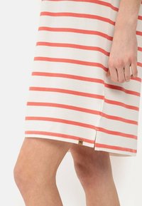 Gestreiftes Kleid mit weißen und korallenfarbenen horizontalen Linien, aus weichem Stoff, mit einem seitlichen Schlitz und einem kleinen Markentag am Saum.