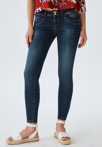 Jeans ajustados de mezclilla en un tono azul oscuro, con una textura suave, que cuentan con costuras naranjas, bolsillos frontales y un cierre de botón.