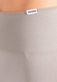 Lichtgrijze geribbelde legging met een gladde tailleband. Een wit label met "SMILODOX" is op de tailleband genaaid. Zachte, rekbare stof.