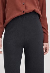 Dunkelgraue Strickhosen mit weicher Textur und elastischem Bund, kombiniert mit einem rostfarbigen Hemd mit Knöpfen.