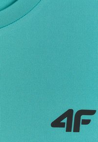 Tissu turquoise avec un col rond et un logo noir « 4F » imprimé près du bord inférieur droit.