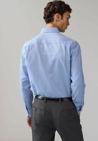 Camicia azzurro chiaro a maniche lunghe con un motivo sottile, abbinata a pantaloni grigio scuro, con una cintura nera lucida.