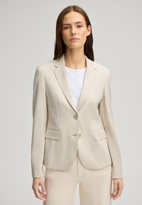 Beżowa marynarka w paski z dwoma guzikami, klapami i bocznymi kieszeniami. Wykonana z lekkiego materiału, charakteryzująca się gładką teksturą.