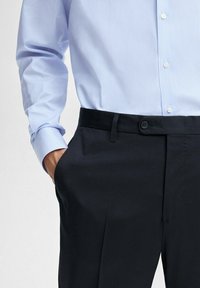 Light blue striped shirt with buttoned cuffs, paired with navy dress pants featuring a front pocket and a button closure.