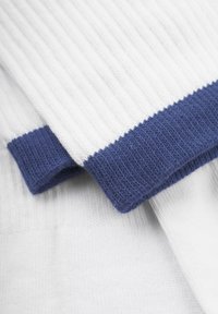 Tejido blanco acanalado con un puño de punto azul marino, que muestra una textura fina y un contraste de color. El diseño enfatiza la simplicidad y la funcionalidad.