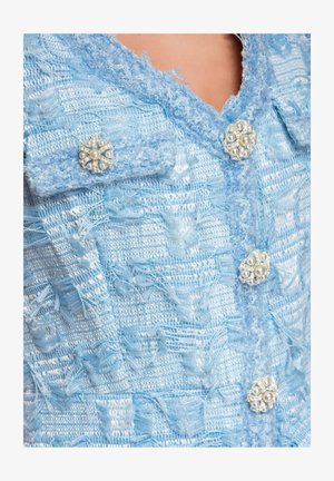 Chaqueta de tela texturizada azul claro con botones en forma de flor de perlas y cristales en el cuello y el frente.