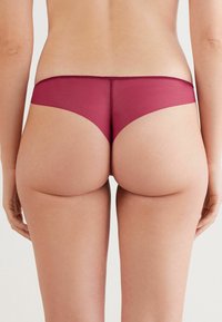 Culotte en dentelle bourgogne avec une finition lisse et une taille élastique, conçue pour un ajustement taille basse avec une couverture minimale.